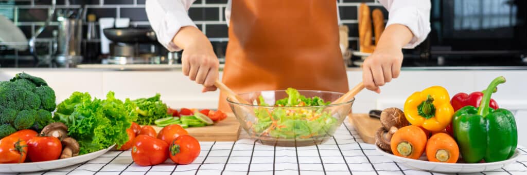 woman in the process of preparing healthy food Vegetable Salad mixing salad wooden spoon in kitchen at home Dieting Concept.
